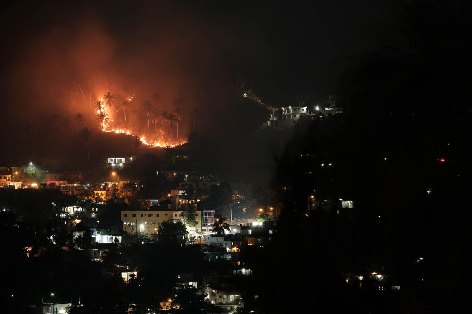 A wildfire burning on hills above a city at night