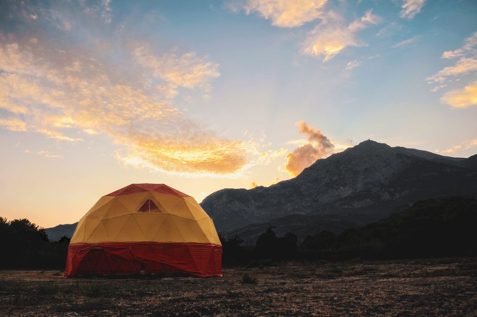 A tent at sunset below desert mountains