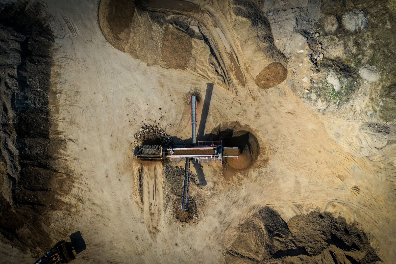 An aerial view of a small open pit with a conveyor cutting through pale desert ground