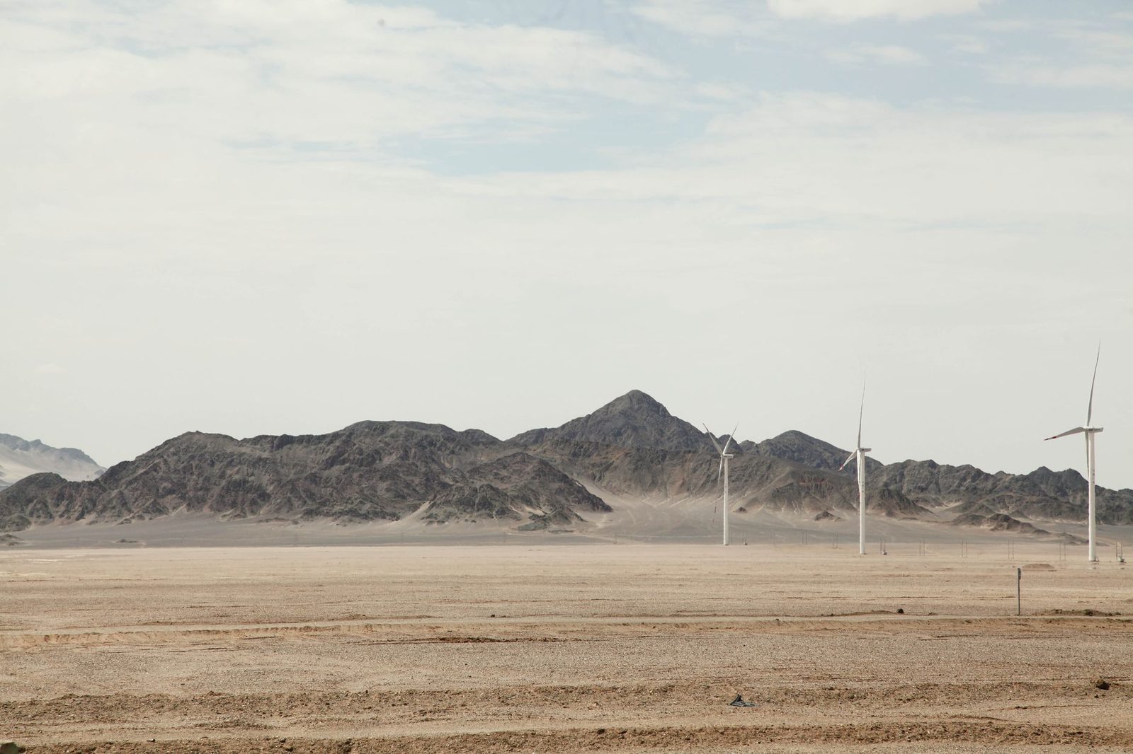 Wind turbines standing on open desert flats below rocky hills