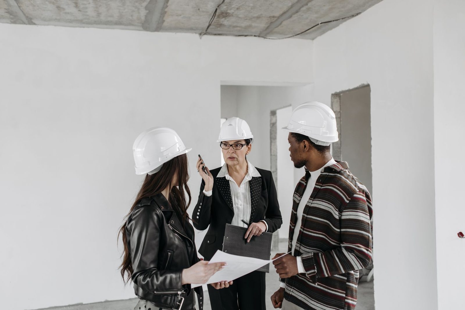 Three people in hard hats reviewing plans in an empty room